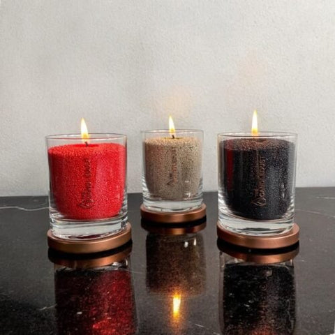 4. Trio of Candledust powder candles in red, beige, and black, burning in glass containers on a black surface