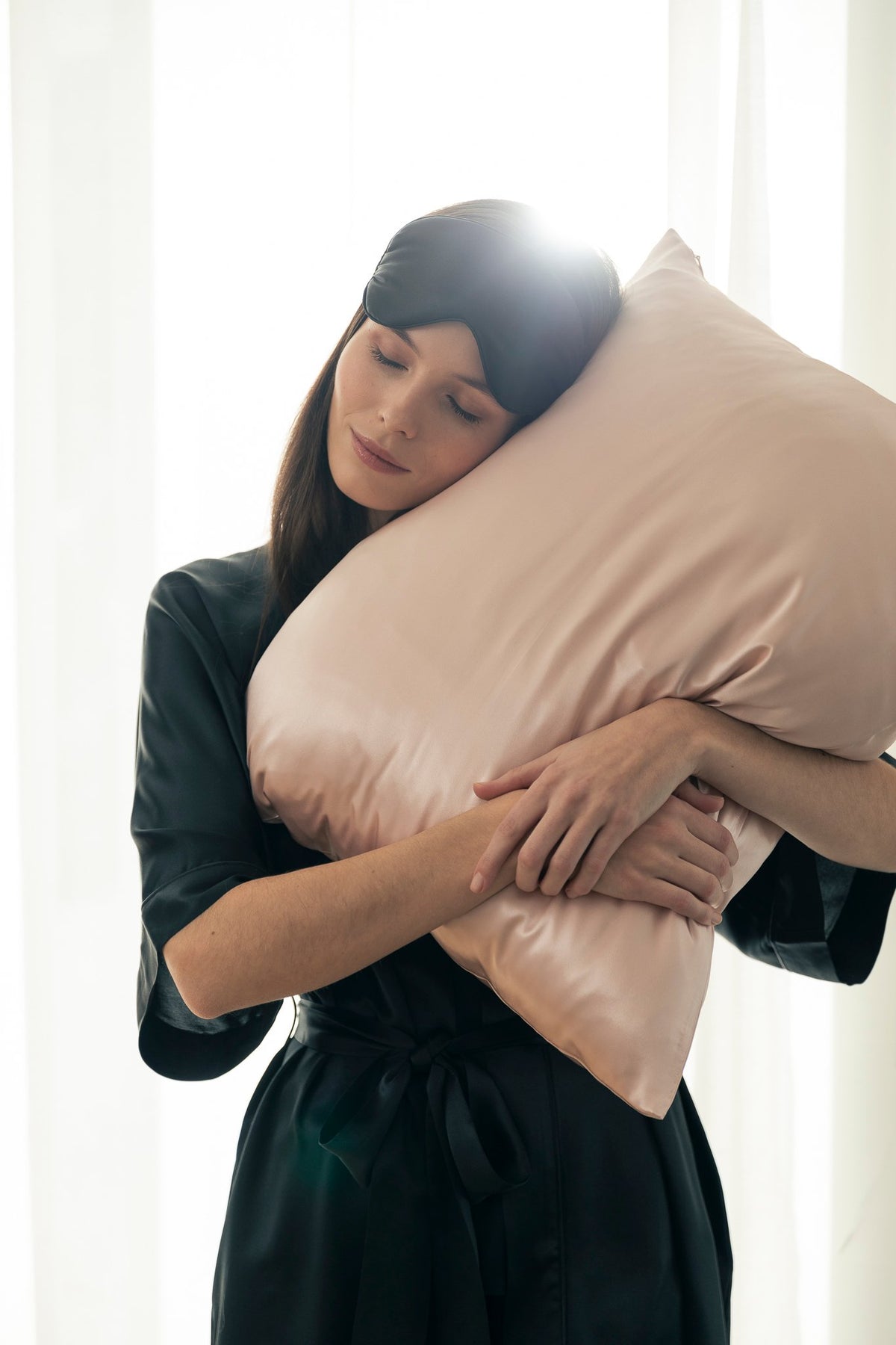 1. Woman embracing pink Mulberry silk pillowcase in a softly lit room, showcasing luxurious texture