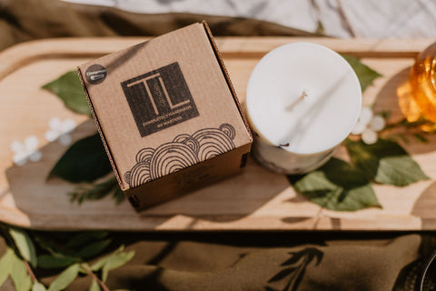 4. Top view of TL Candles box and white soy wax candle on wooden tray with leaves