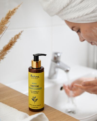 1. Woman using Nurme Neroli Purifying Cream Cleanser at bathroom sink, showcasing skincare routine