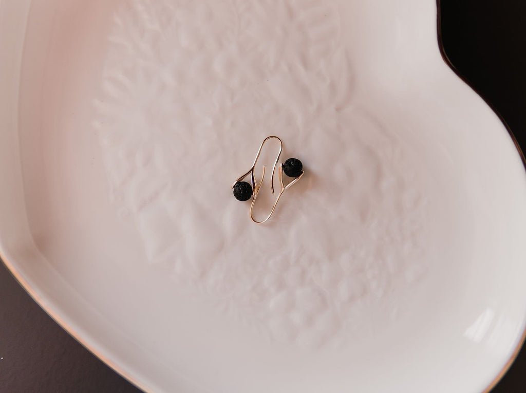 2. Flat lay of Canary Lava 14K gold-plated diffuser earrings with black lava beads on white dish
