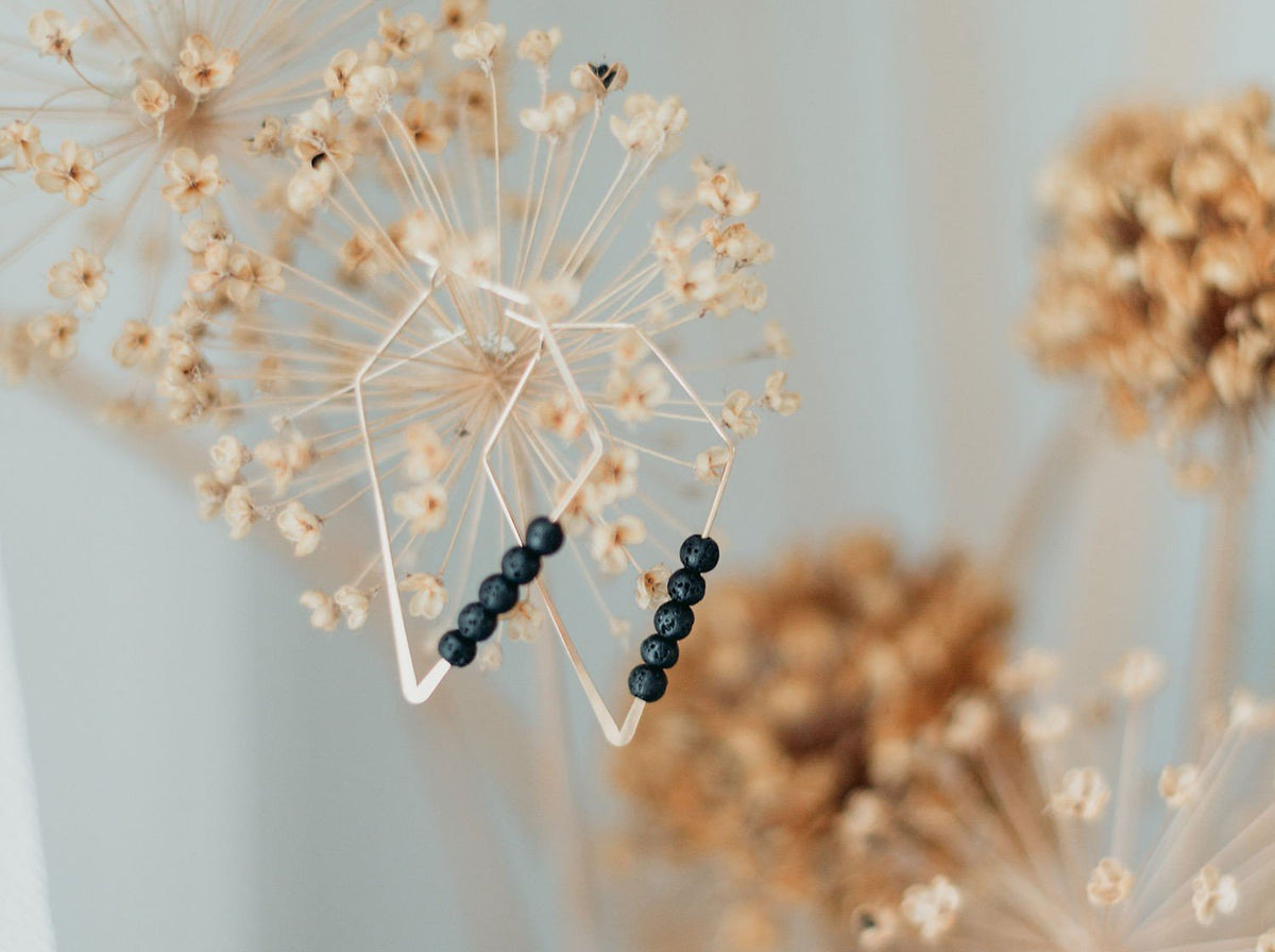 2. Canary Lava 14K gold plated diffuser earrings with rhombus design and lava beads, displayed on dried flowers