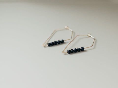 3. Studio shot of Canary Lava 14K gold plated diffuser earrings with rhombus design and lava beads, laid flat