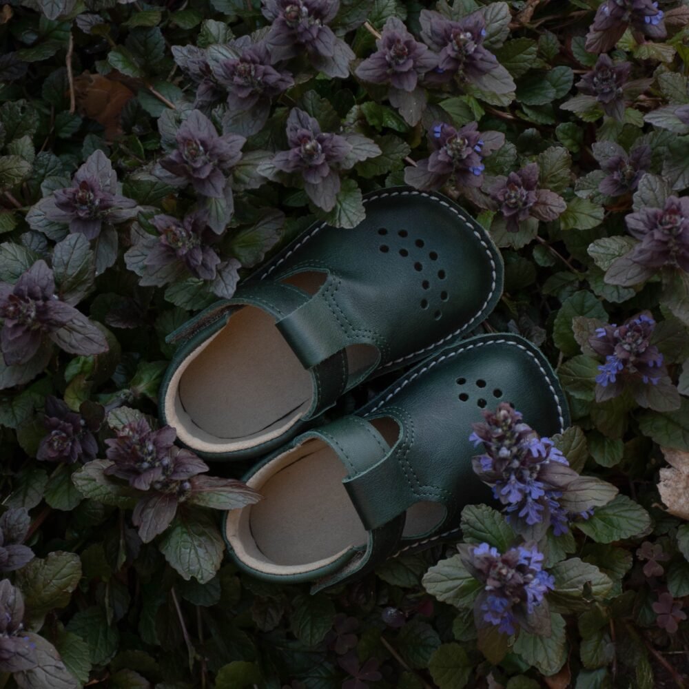 1. Dark green Lusti leather kids' shoes by Omaking placed among purple flowers, showcasing natural setting