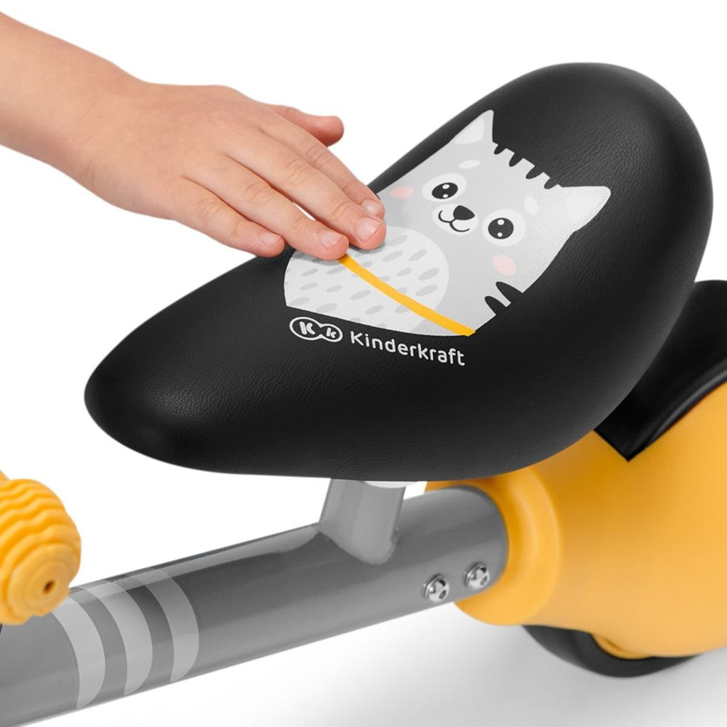 12. Close-up of Kinderkraft CUTIE balance bike saddle with kitten print and child's hand