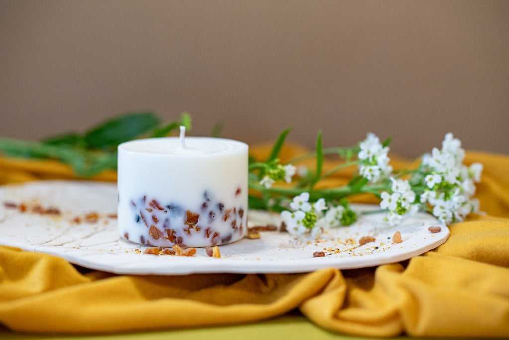 8. Single TL Candles soy wax candle with amber pieces on decorative plate, surrounded by flowers, highlighting pine scent