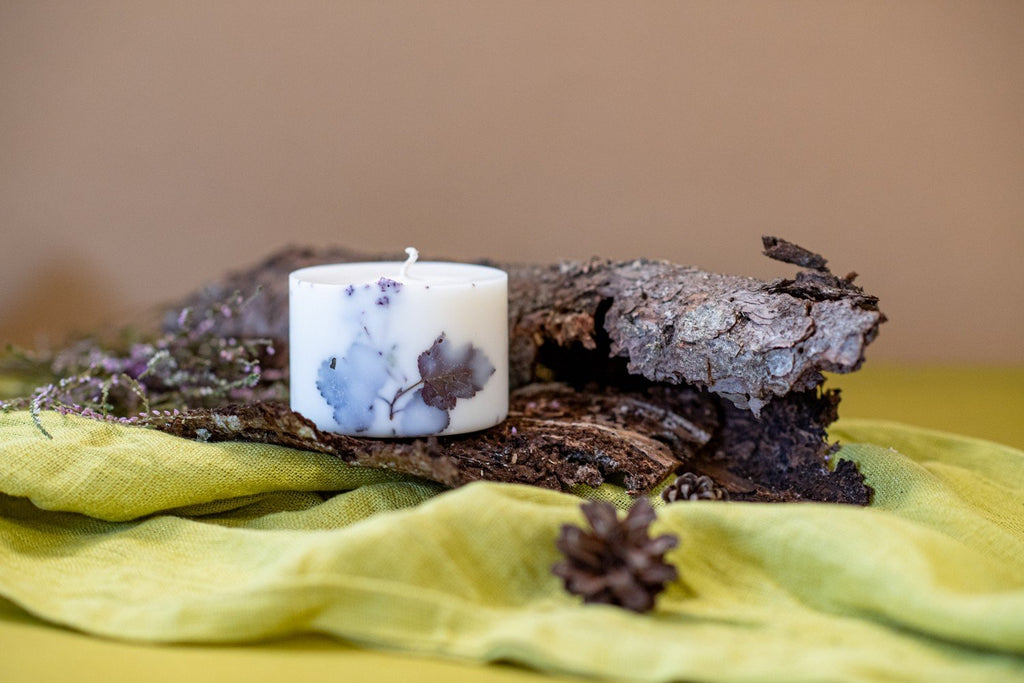 4. Hand-made white soy wax candle with forest scent, detailed with natural elements, placed on bark and green fabric