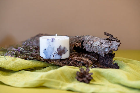 4. Hand-made white soy wax candle with forest scent, detailed with natural elements, placed on bark and green fabric