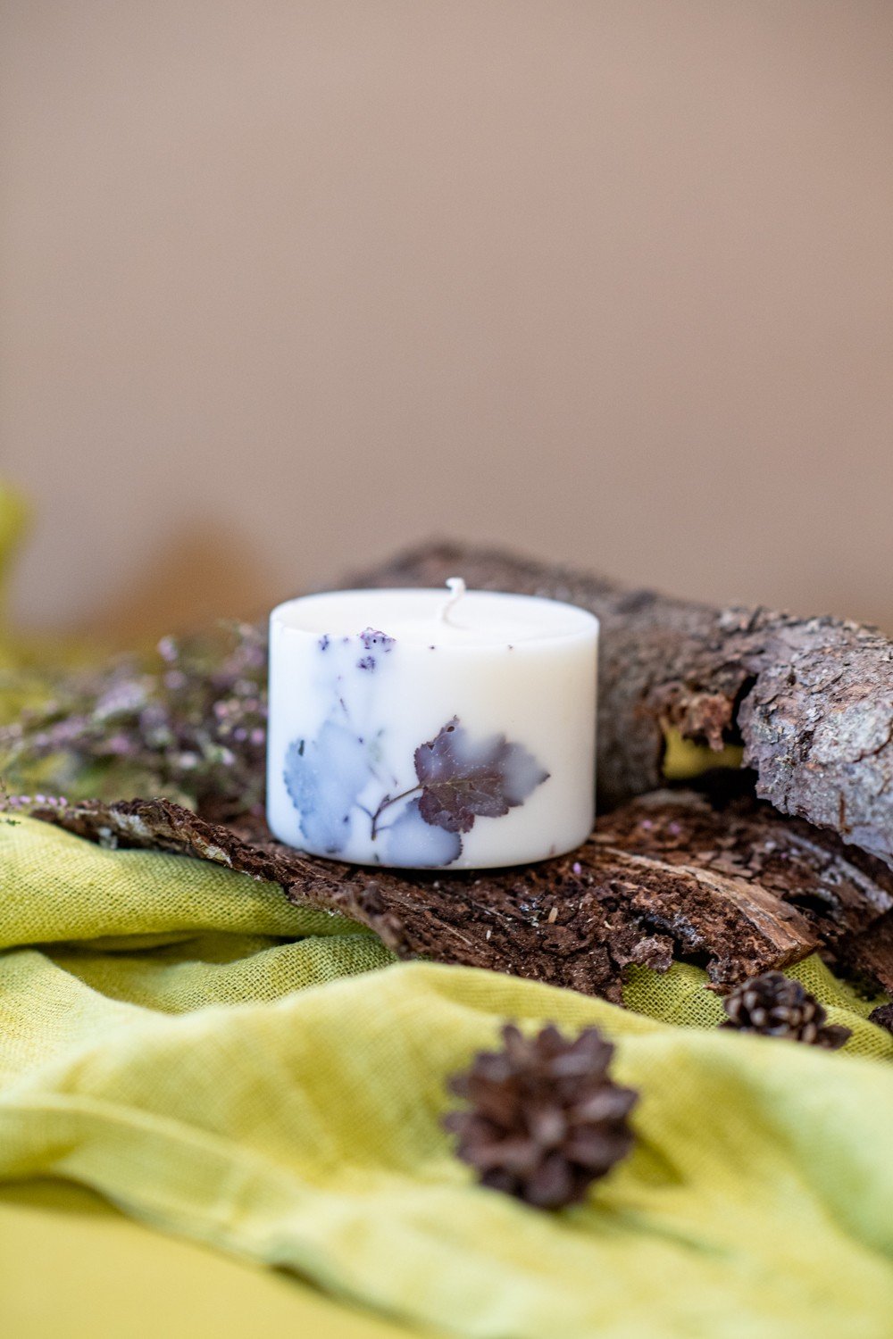 2. Hand-made white soy wax candle with forest scent, featuring natural decor, set on bark with green fabric
