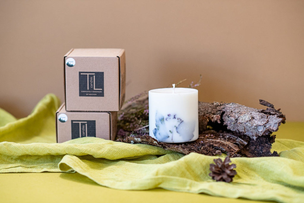 6. Hand-made white soy wax candle with forest scent, alongside TL Candles packaging, on bark and green fabric