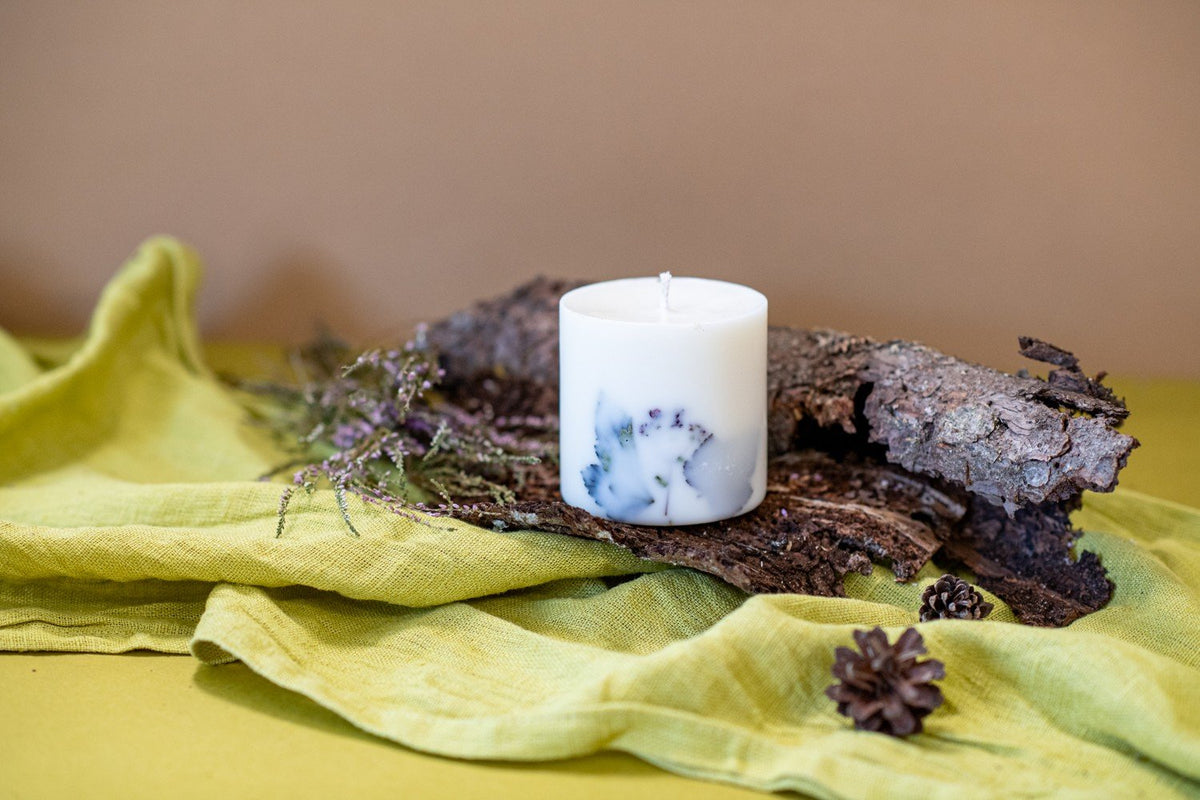 5. Hand-made white soy wax candle with forest scent, decorated with natural elements, resting on bark and green fabric