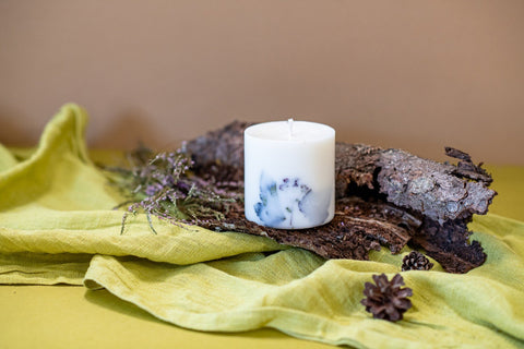 5. Hand-made white soy wax candle with forest scent, decorated with natural elements, resting on bark and green fabric