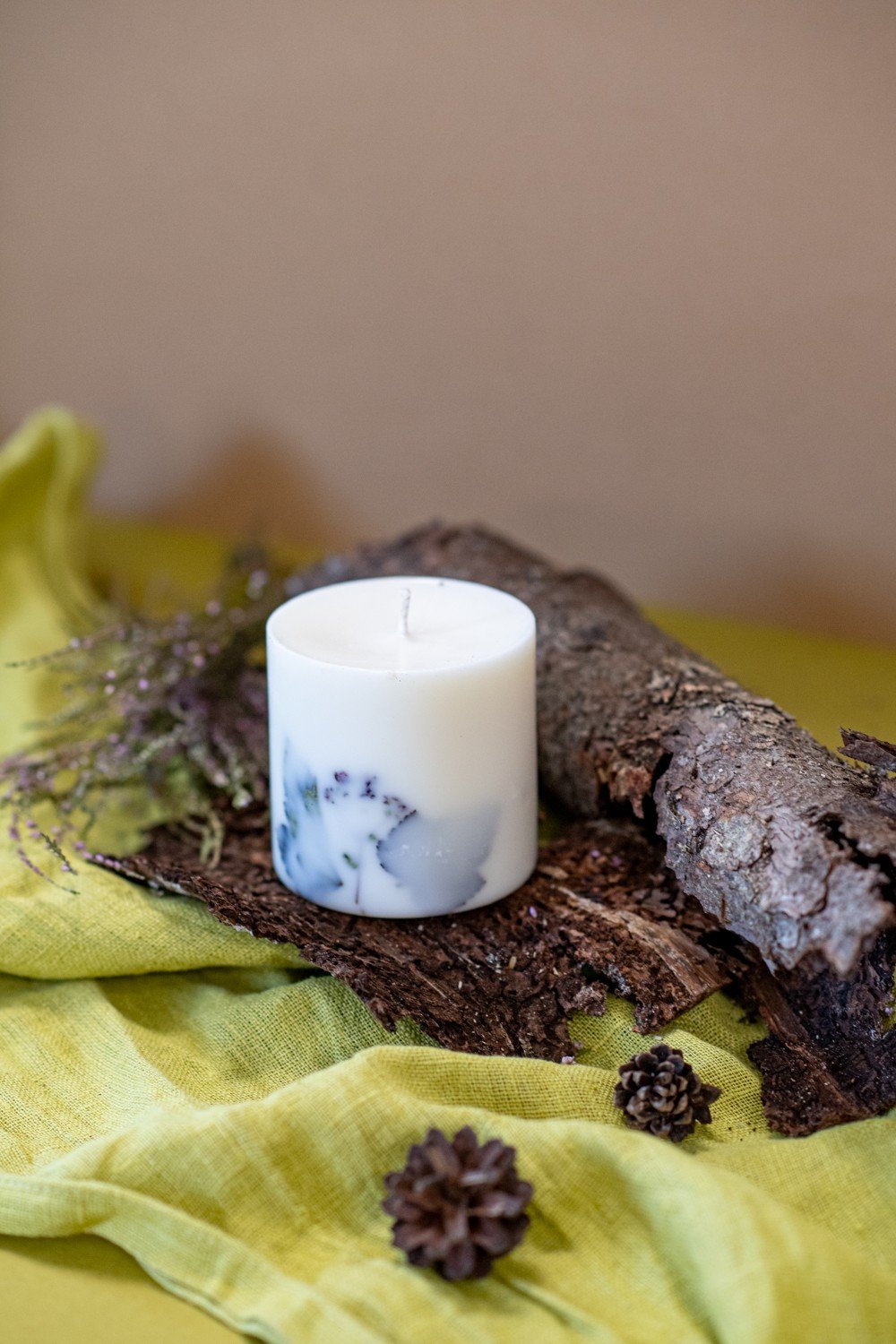 1. Hand-made white soy wax candle with forest scent, adorned with natural elements, displayed on bark and green fabric
