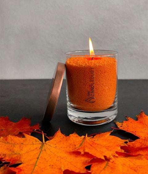2. Candledust unscented orange powder candle in glass, lit with autumn leaves, showcasing vibrant color and flame