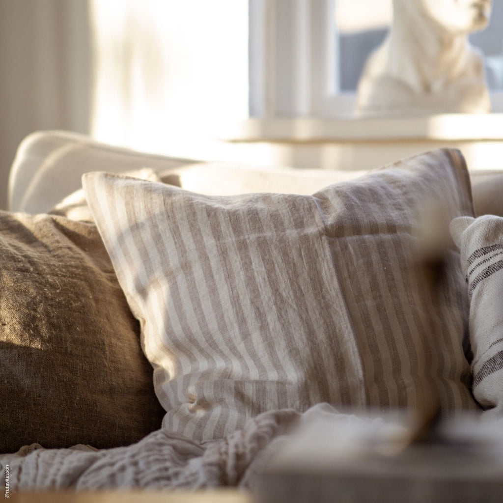 2. Beige and white striped Linen Tales cushion cover on a cozy sofa with warm lighting