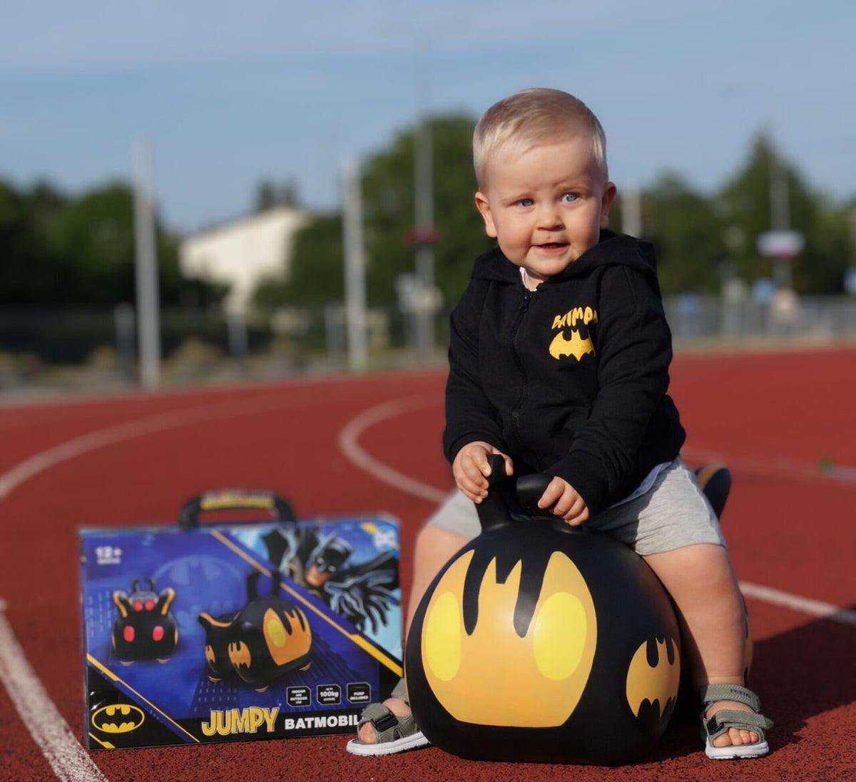 2. Toddler in black hoodie on JUMPY Batmobile toy with product box on red track