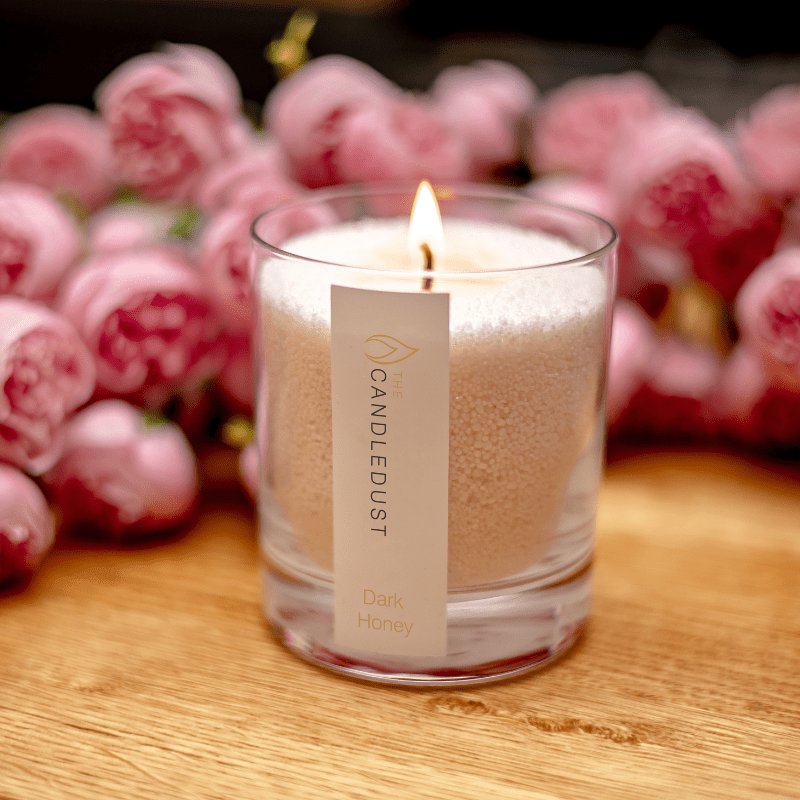 6. Candledust Dark Honey powdered candle lit with pink roses in background, highlighting romantic setting