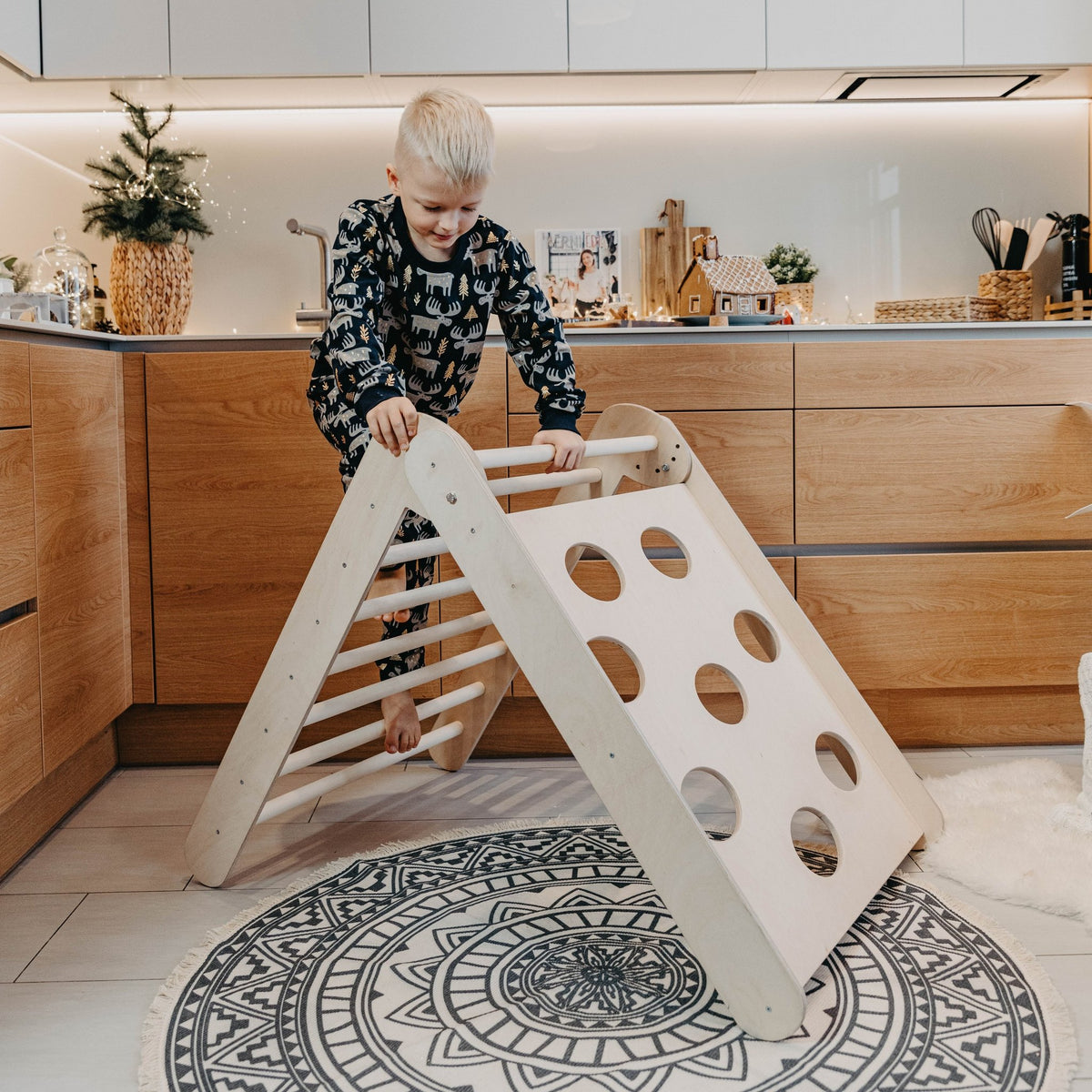 1. Boy in animal print pajamas climbing Montessori triangle in a kitchen setting