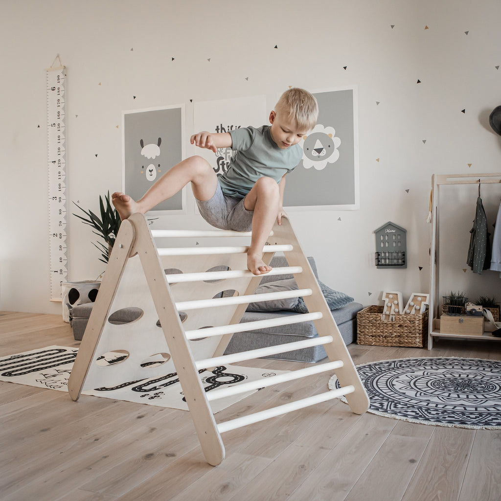 1. Boy in grey shorts climbing Montessori triangle in a playroom with wall decor