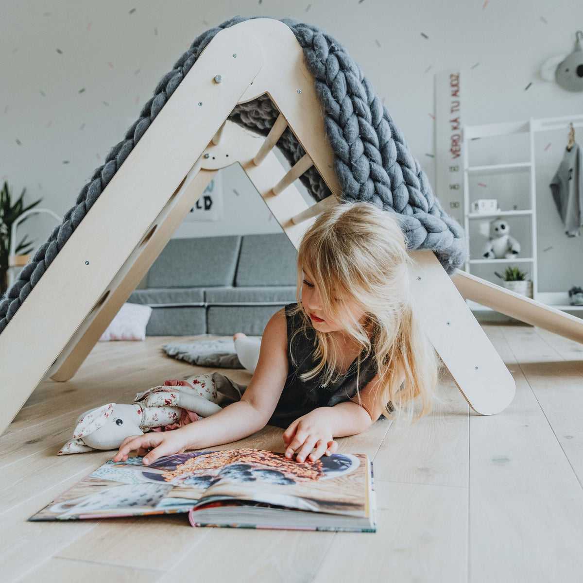 1. Girl reading under Montessori climbing triangle draped with a grey blanket in a playroom