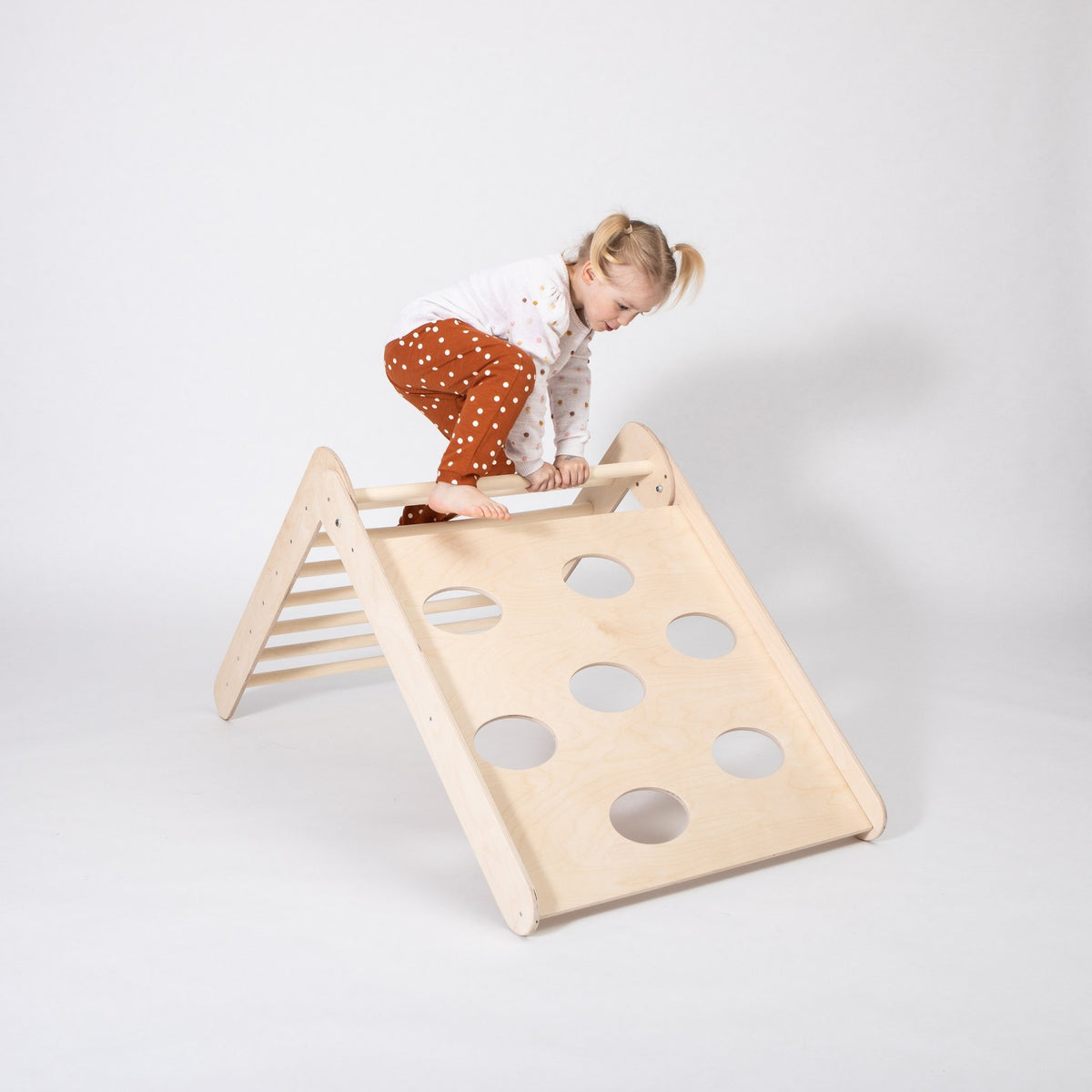 1. Young girl in polka dot pants climbing up Montessori triangle in a bright room