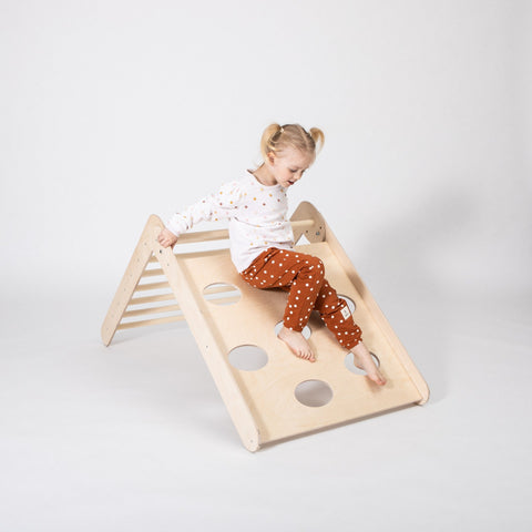1. Young girl in polka dot pants climbing down Montessori triangle in a bright room