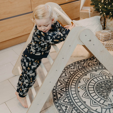 1. Toddler in animal print pajamas climbing Montessori triangle in cozy indoor setting