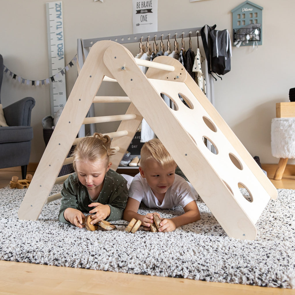 1. Two children playing under Montessori climbing triangle on a soft rug in a playroom