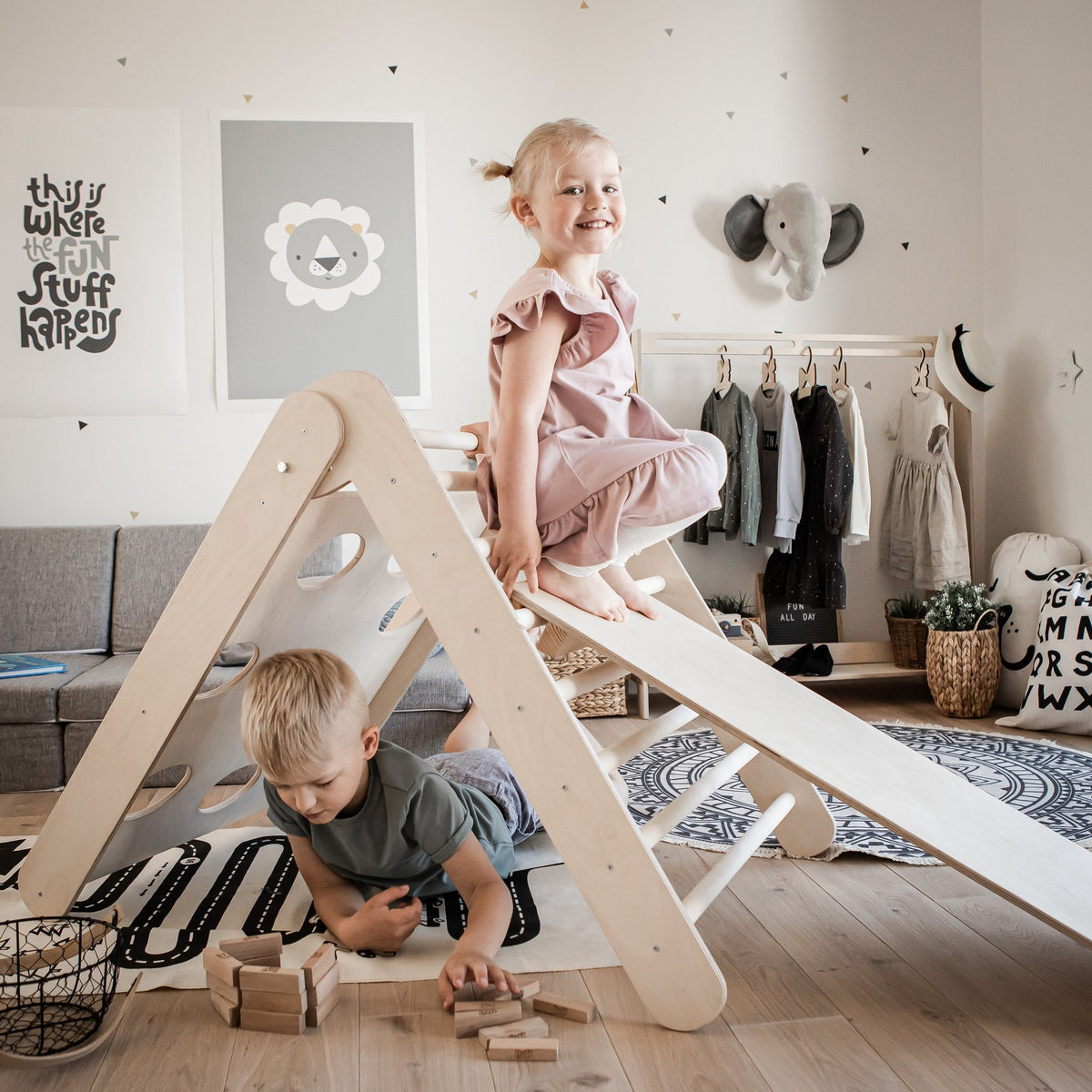 1. Two children playing on Montessori climbing triangle with ramp in a cozy playroom, girl sliding down ramp, boy playing with blocks underneath.