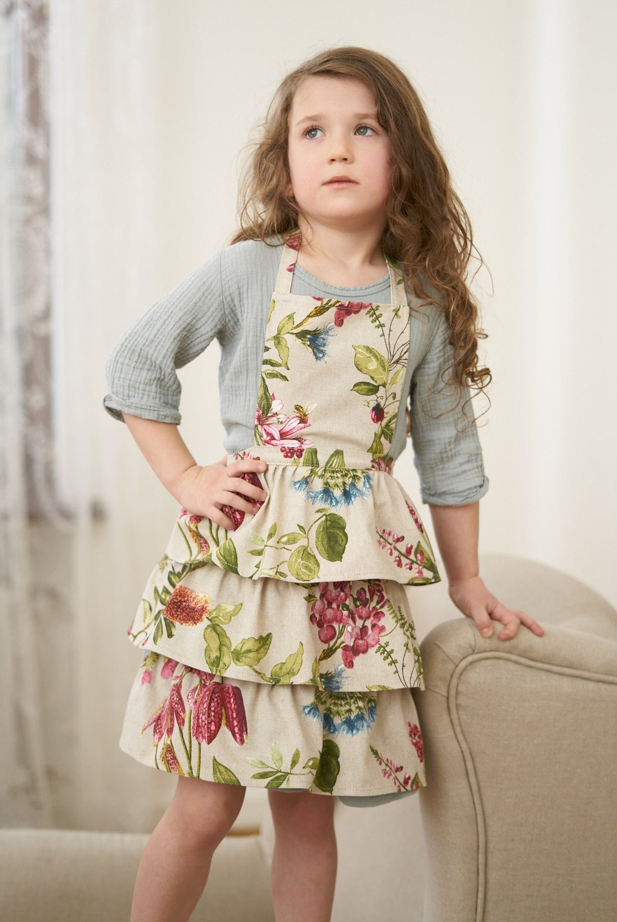 2. Girl wearing Botanico Kids Apron by Hortensias Home, featuring a vibrant floral pattern in a lifestyle setting