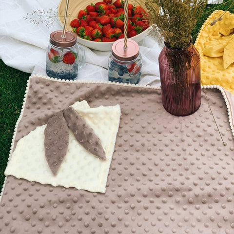 3. Beige textured blanket with bunny ears comforter on grass, next to strawberries and drinks