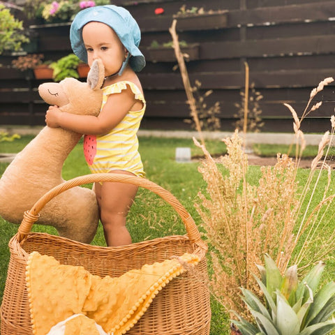1. Child in yellow outfit hugging rusty brown alpaca soft toy-pillow in garden setting
