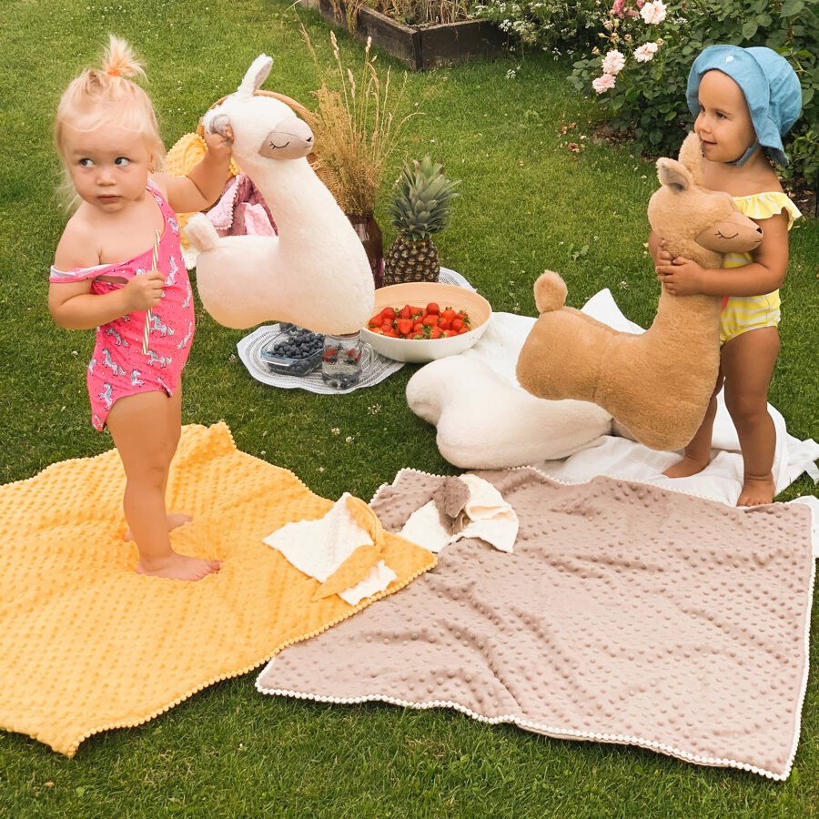 4. Two toddlers playing on yellow and beige textured blankets with plush toys in a garden setting