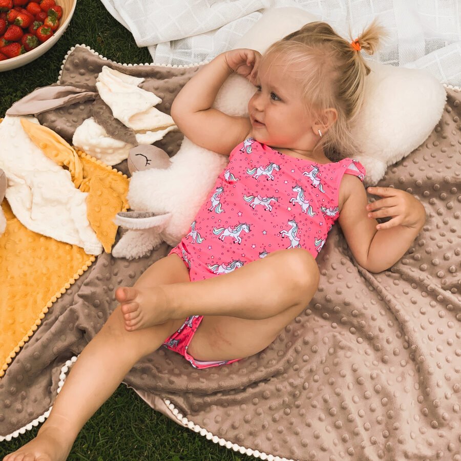 3. Child lounging on a cream alpaca soft toy-pillow on a textured blanket with strawberries in a garden