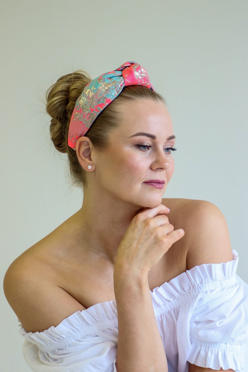 1. Woman wearing Eva Oherjus Knot Headband Misty with neon pink, gold, and mint green abstract design