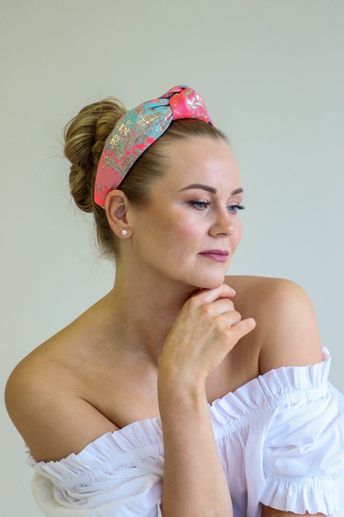 1. Woman wearing Eva Oherjus Knot Headband Misty with neon pink, gold, and mint green abstract design