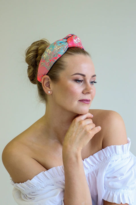 1. Woman wearing Eva Oherjus Knot Headband Misty with neon pink, gold, and mint green abstract design