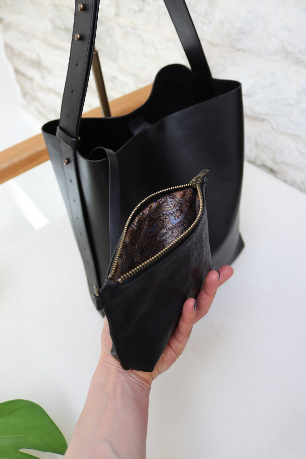 5. Close-up of Tairi Roosve black leather tote with removable clutch being held, highlighting interior suede lining