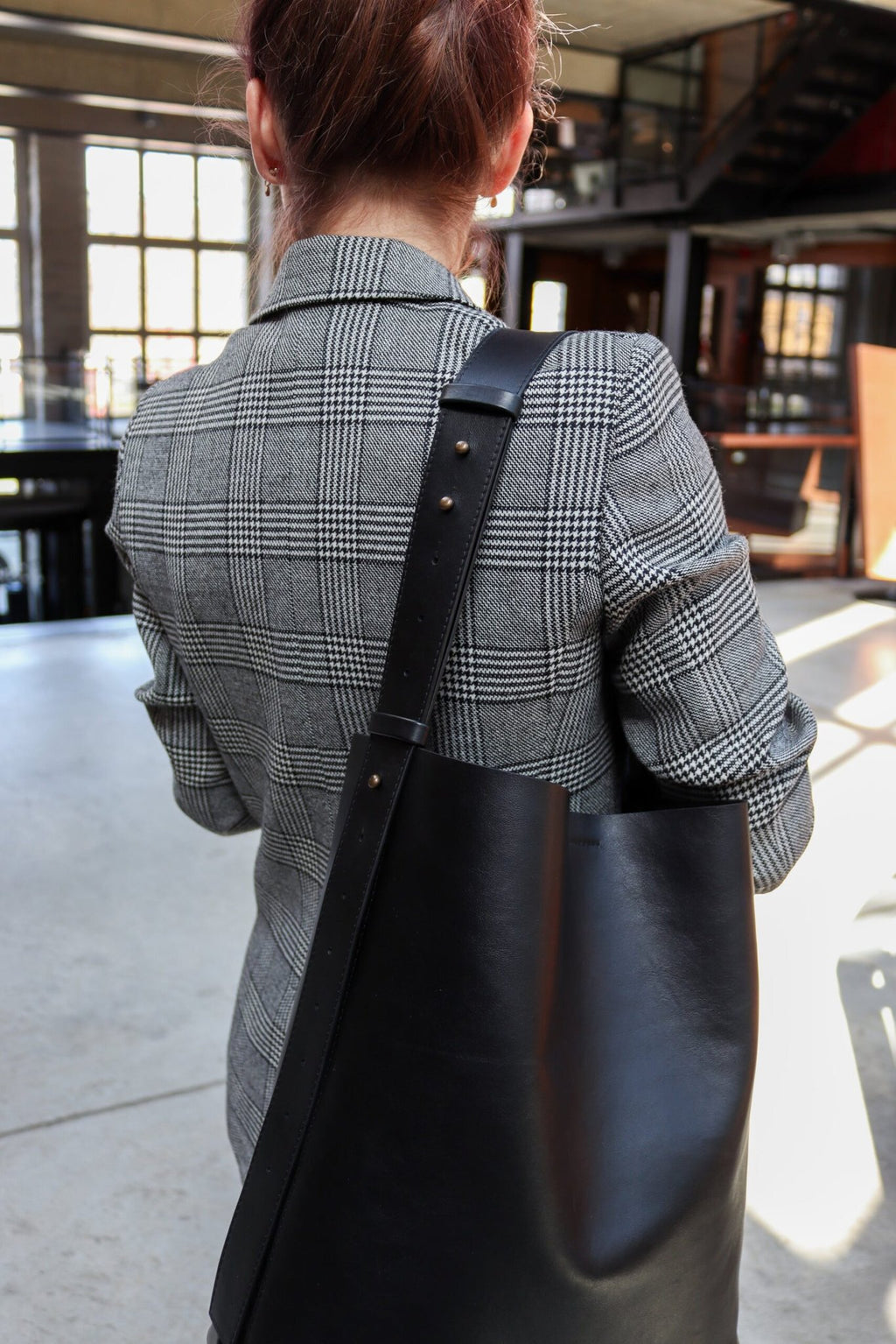 2. Back view of woman with Tairi Roosve black leather tote bag, showcasing adjustable strap in a stylish environment