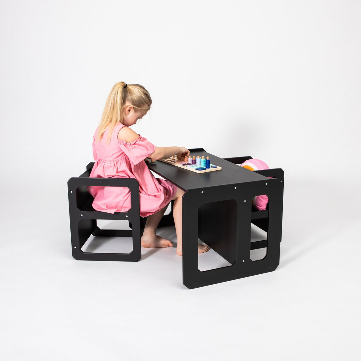 11. Girl in pink dress playing at black Montessori weaning table and chair set on white background