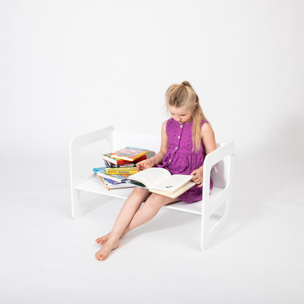 7. Girl in purple dress reading on a white Montessori chair with books stacked beside her