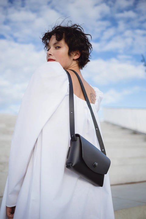 2. Woman in white dress showcasing Mirgoods black leather clutch bag from the back