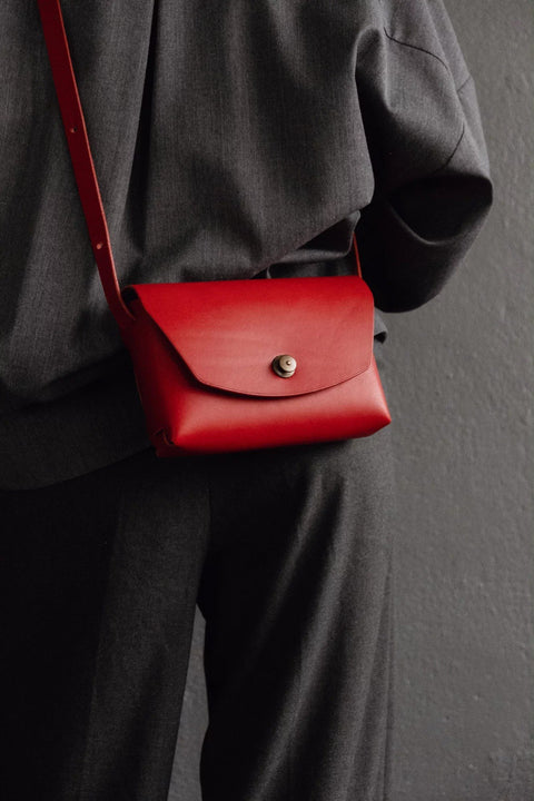 1. Women's red leather clutch bag by Mirgoods worn crossbody, shown in lifestyle setting