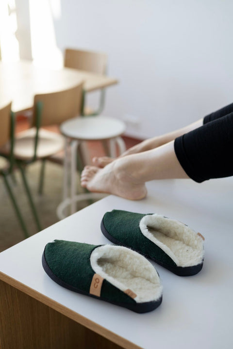 3. Unisex dark green TOKU Brussels slippers by Omaking on a table with a woman stretching nearby