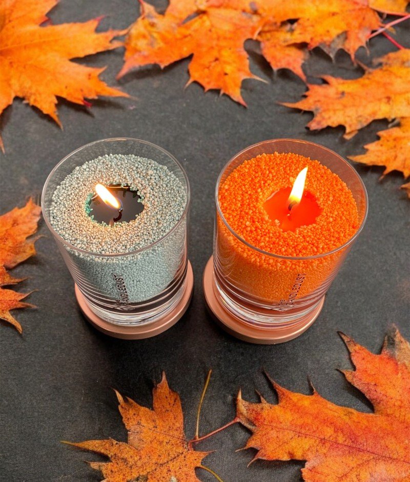 4. Pair of Candledust unscented powder candles in orange and grey, lit in glass containers with autumn leaves