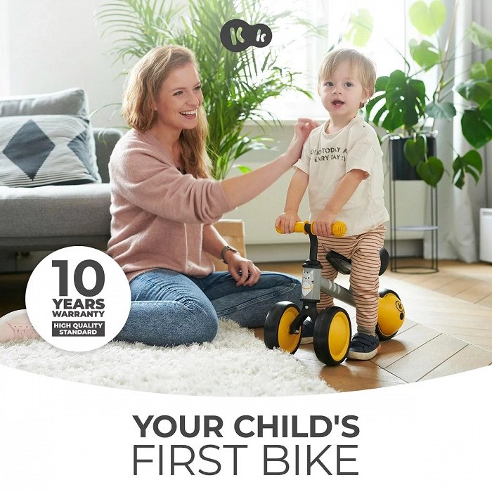 7. Child on yellow Kinderkraft CUTIE balance bike with parent indoors, highlighting first bike experience