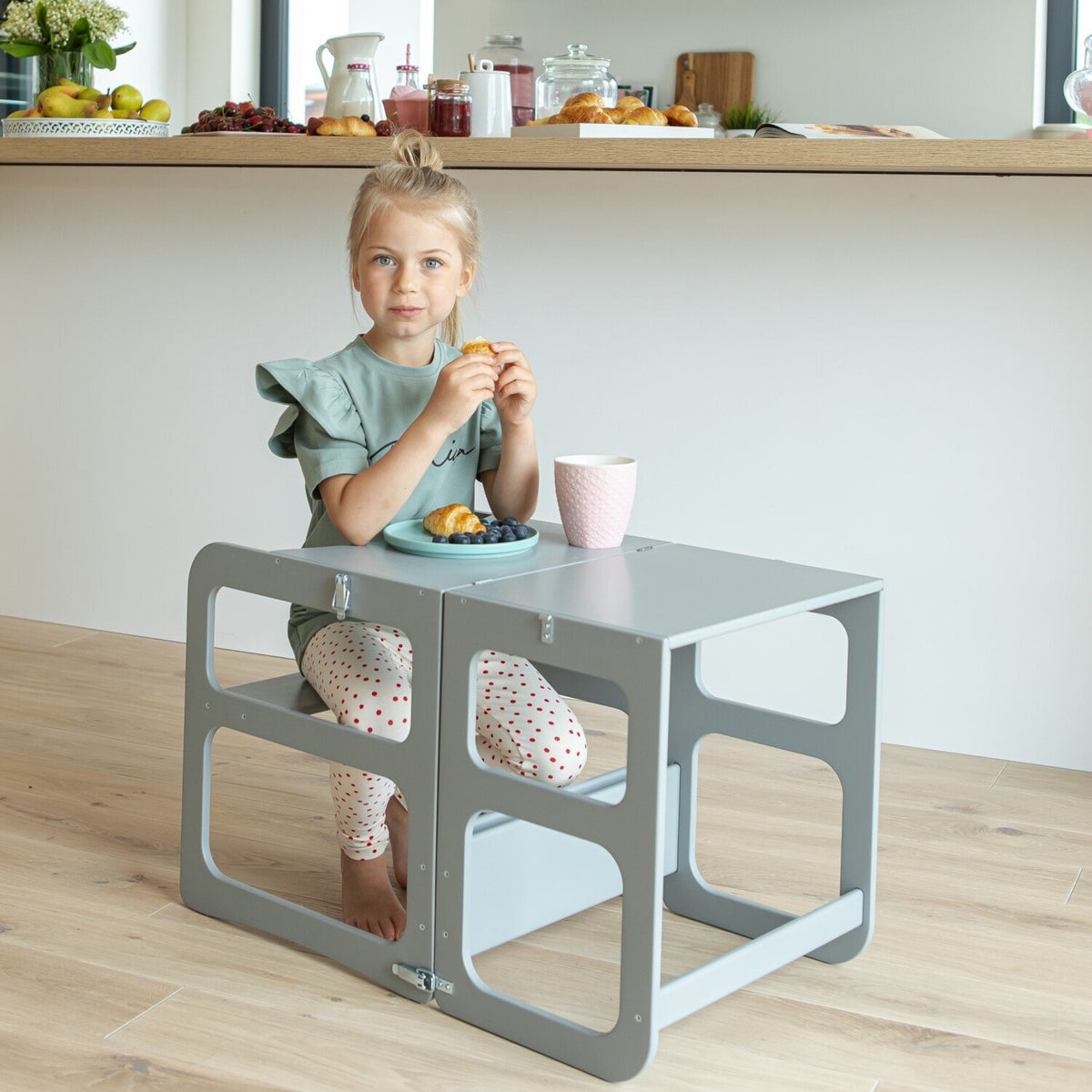 13. Girl sitting at grey kitchen tower in table mode, having a snack in a bright kitchen