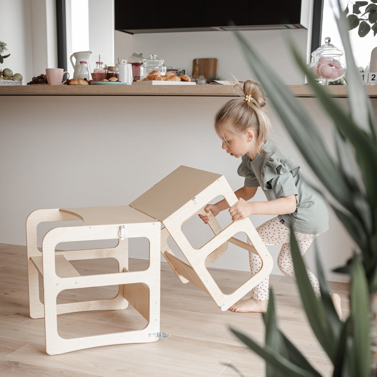 2. Child converting natural wood kitchen tower into table and chair set in a modern kitchen