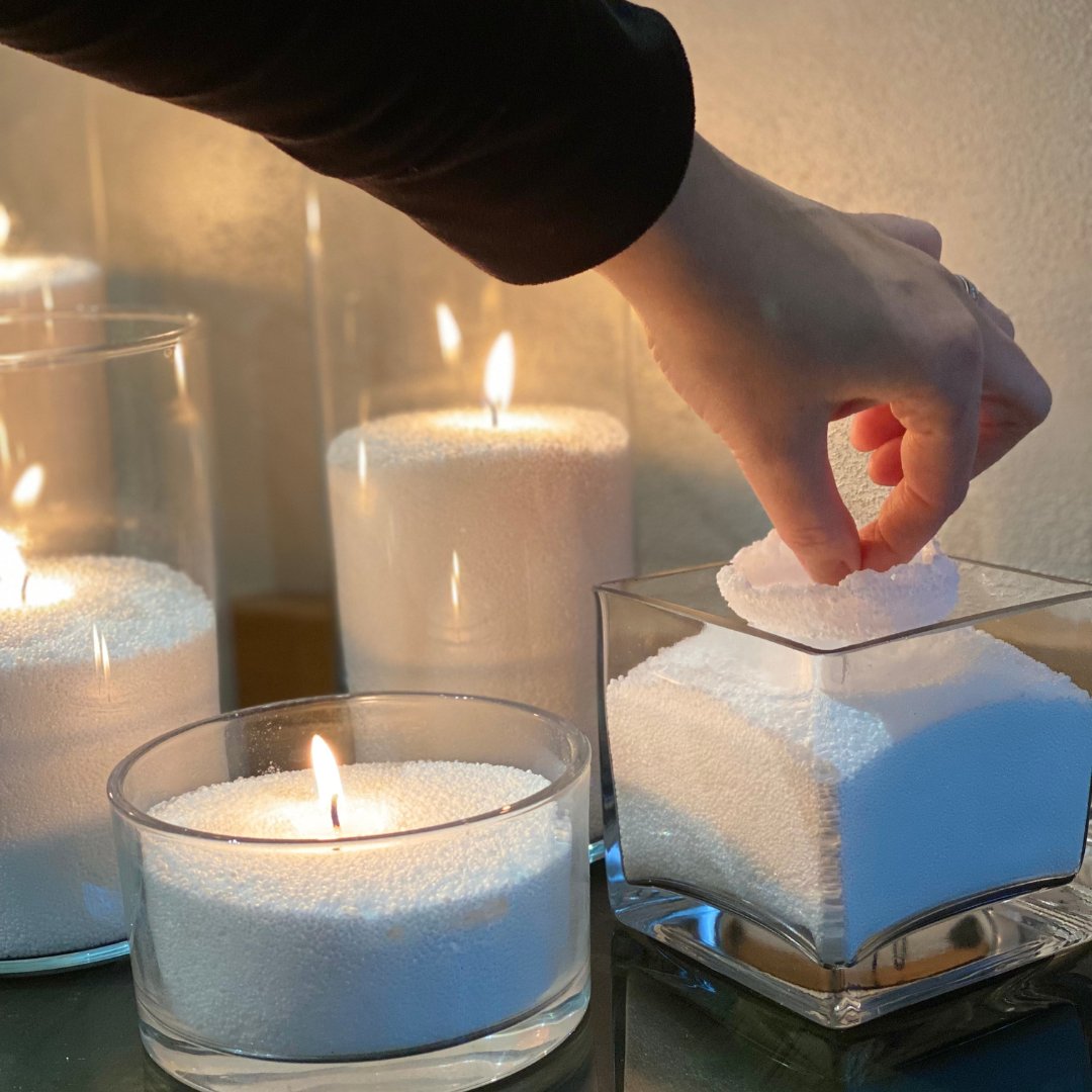 1. Hand placing wick in Candledust powder candle, surrounded by glowing candles in glass containers