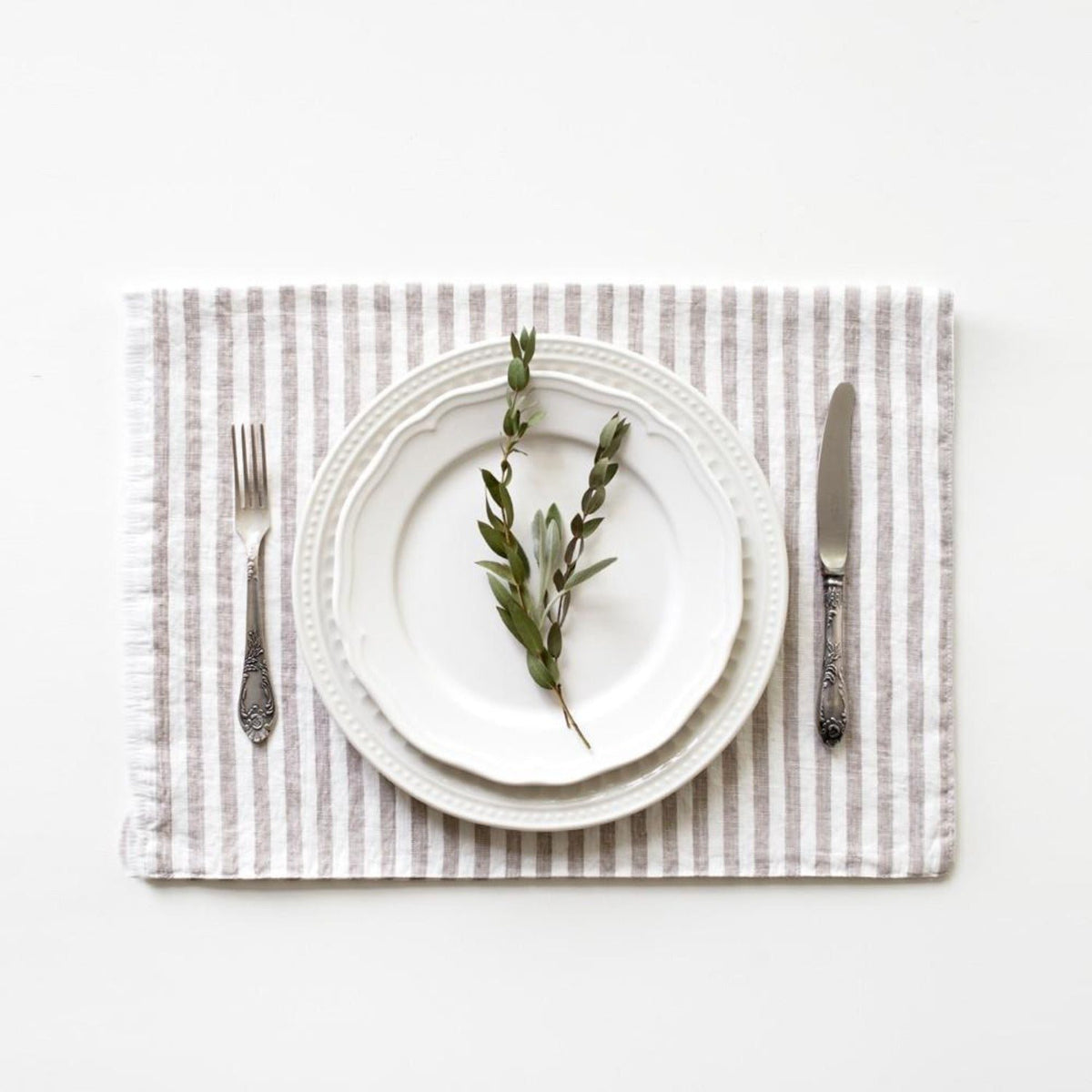 2. Striped linen placemat with a sprig of greenery on a white plate, set with a fork and knife